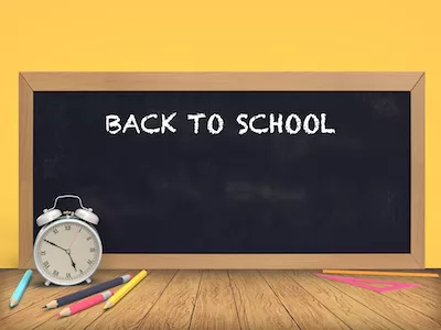 Blackboard with alarm clock and pencils on yellow background